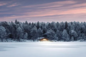 Casa iluminada al borde de un lago helado al atardecer en Rovaniemi, Laponia.