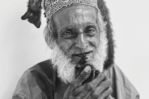 Retrato de un hombre mayor con gorro tradicional y un lémur sobre su cabeza, en Stone Town, Zanzíbar.
